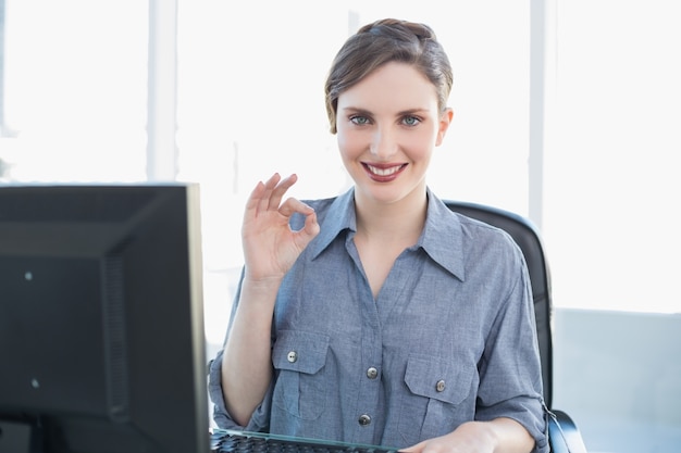 Lovely jovem empresária fazendo um gesto sentado em sua mesa