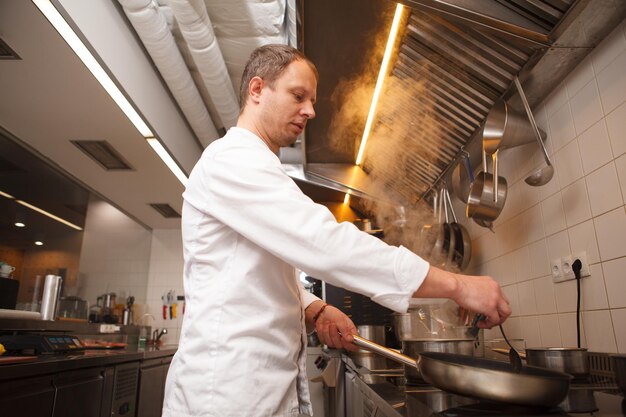 Foto low angle shot eines professionellen kochs, der mit bratpfanne kocht