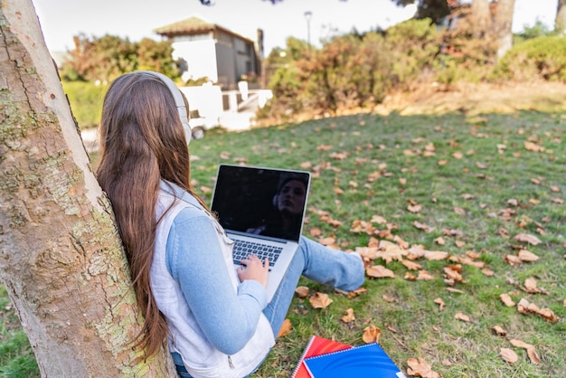 Foto low angle view eines teenagers mit ihrem computer auf einem baum sitzend mit ihren vorräten neben ihr