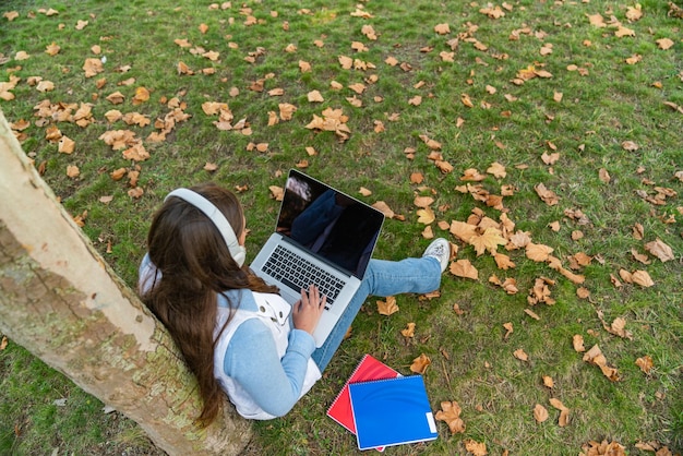 Low Angle View eines Teenagers mit ihrem Computer auf einem Baum sitzend mit ihren Vorräten neben ihr