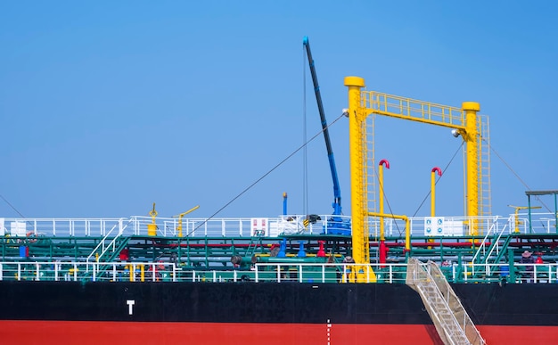 Ölpipelinesystem mit Kranmaschinen im Tankschiff, während es am Hafen gegen den blauen Himmel festgemacht ist