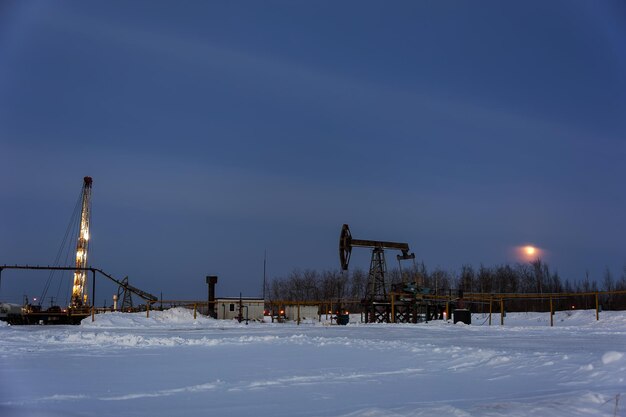 Ölpumpenheber auf einem Ölfeld. Wintersonnenunterganghimmelhintergrund. Gewinnung von Öl. Erdöl-Konzept.