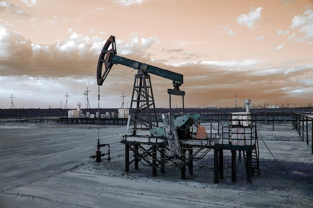 Ölpumpenheber und Bohrlochkopf mit Ventilanker während des Sonnenuntergangs auf dem Ölfeld. Gewinnung von Öl. Öl- und Gaskonzept. Getönt.