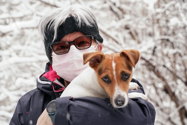 Ältere ältere Frauen, die warme Kleidung und eine Einweg-Virusmaske tragen, halten ihren Hund an den Händen. Leben während der wintersaison coronavirus covid-19 ausbruchsillustration