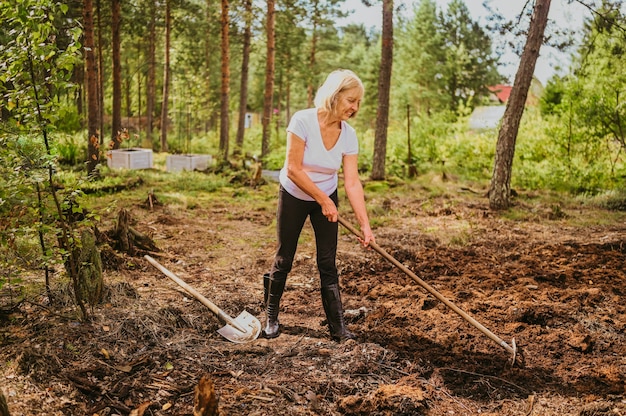 Ältere ältere Gärtnerin, die im Freien auf der Sommerfarmlandschaft mit fürsorglichem Boden gräbt