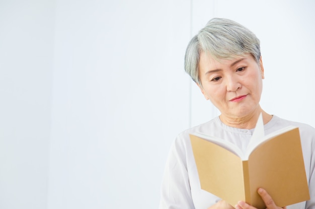 Ältere Asia-Frau liest Buch auf weißem Hintergrund.