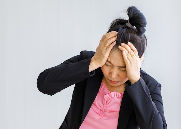 Ältere Asiatin mittleren Alters, die Schmerzen verspürt und unter plötzlichen Kopfschmerzen und Hirnschlagattacken leidet und ihren Kopf mit gestresstem Gesicht hält. Konzept des Gehirn- und Kopfproblems.