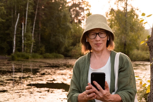 Ältere asiatische Frau, die das Telefon für Videoanrufe benutzt, die im Stadtpark spazieren gehen