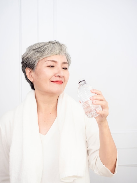 Ältere asiatische Frau, die eine Pause beim Training zu Hause macht. Athletische reife Frau, die eine Flasche Wasser hält.