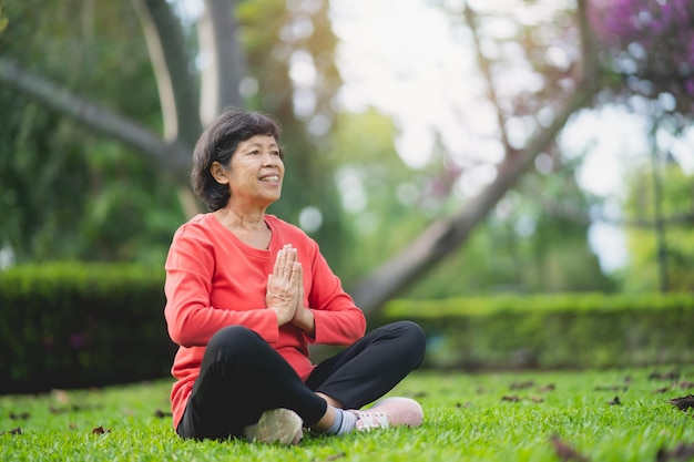 Ältere asiatische Frau, die Yoga-Unterricht praktiziert und im Garten meditiert. Ausarbeiten Wellness-Konzept