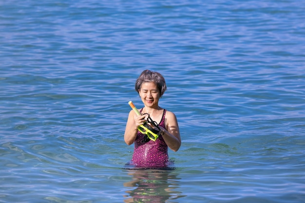 Ältere asiatische Frau mit einer Maske zum Schnorcheln im Meer