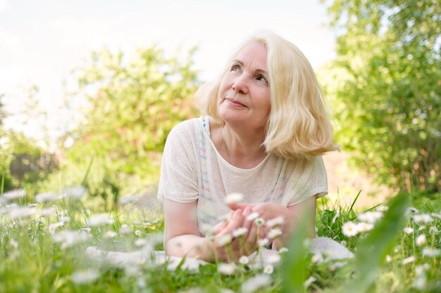 Ältere blonde Frau, die sich im Sommer im Gras ausruht