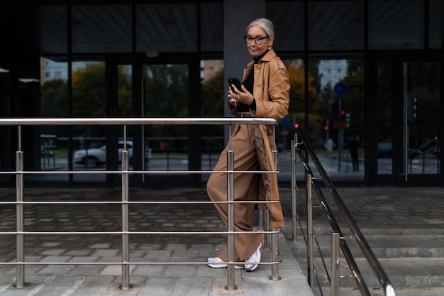 Ältere erwachsene Geschäftsfrau auf dem Hintergrund des Eingangs zum Bürogebäudejahr alt