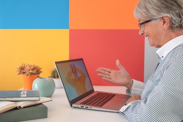 Ältere Frau amüsiert Video-Chat mit einem Freund per Laptop Reife Frau lacht, während sie mit einem entfernten Mann spricht, der die Hände in seinem Haar hat Farbiger Hintergrund