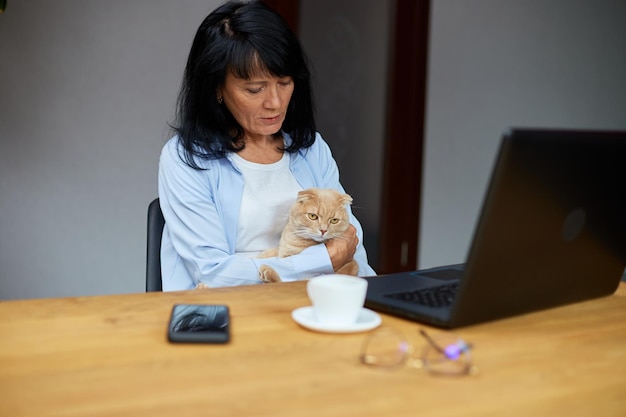 Ältere Frau arbeitet an einem Notebook-Laptop und hält Katze