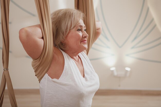 Ältere Frau, die Aerial Yoga im Sportstudio praktiziert