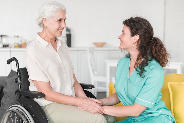 Ältere Frau, die auf dem Rollstuhl hält die Hand der Krankenschwester sitzt