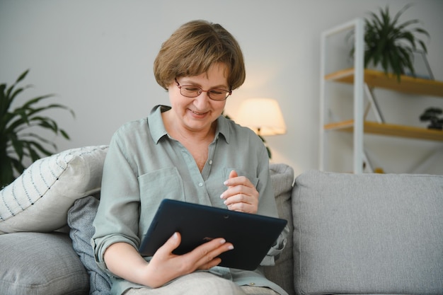 Ältere Frau, die auf dem Sofa über ihr digitales Tablet schaut und lacht