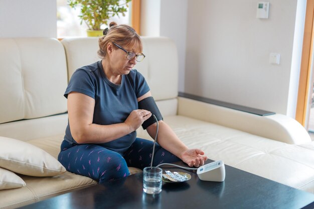Ältere Frau, die den Blutdruck zu Hause überprüft Ältere Frau, die an Bluthochdruck leidet, sitzt auf einer Couch und verwendet ein Pulsometer-Tonometer