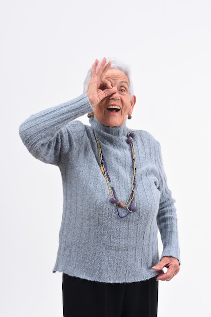 Ältere Frau, die durch Finger schaut, als ob tragende Gläser auf weißem Hintergrund