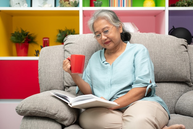 Ältere Frau, die ein Buch liest, genießen und entspannen, allein zu Hause bleiben und den Ruhestand genießen