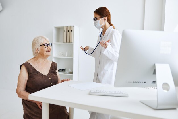 Ältere Frau, die eine medizinische Maske bei der Untersuchung durch ein Krankenschwester-Stethoskop trägt