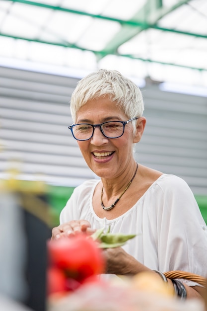 Ältere Frau, die frisches organisches Gemüse auf Markt kauft