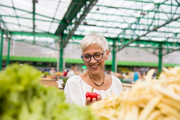 Ältere Frau, die frisches organisches Gemüse auf Markt kauft