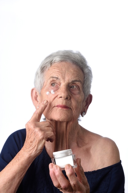 Ältere Frau, die Hautcreme oder Feuchtigkeitscreme an ihrem Gesicht aufträgt