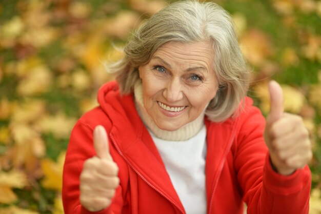 Ältere Frau, die im Herbst im Park Daumen zeigt