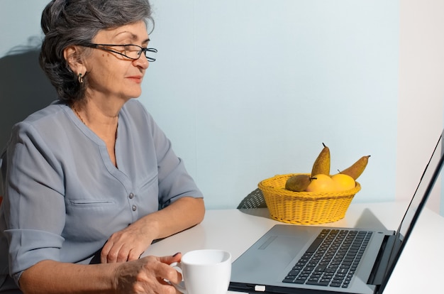 Ältere Frau, die Kaffee trinkt und jemanden online auf Laptop zu Hause spricht. Videoanrufkonzept, neue Normalität, Selbstisolation