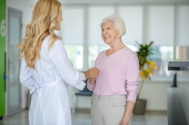 Ältere Frau, die mit dem Arzt im Korridor der Klinik spricht und ihre Hand hält