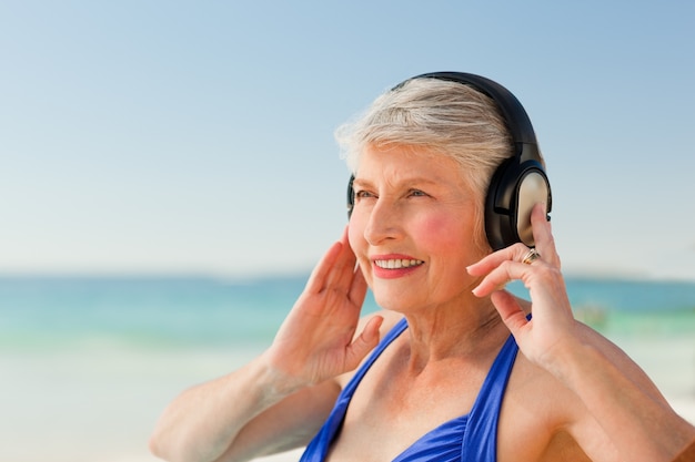 Ältere Frau, die Musik am Strand hört