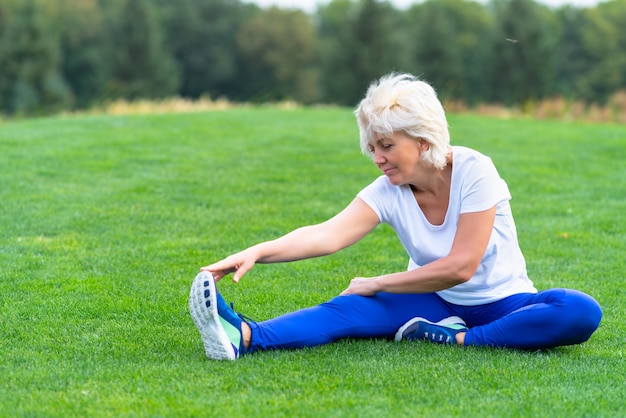 Ältere Frau, die Sportkleidung trägt, die auf grünem Gras im Park ausübt