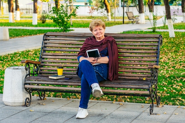 Ältere Frau, die Tablette liest E-Book in einem Park verwendet