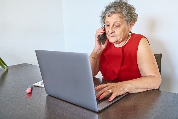 Ältere Frau, die telefoniert, während sie zu Hause einen Laptop benutzt