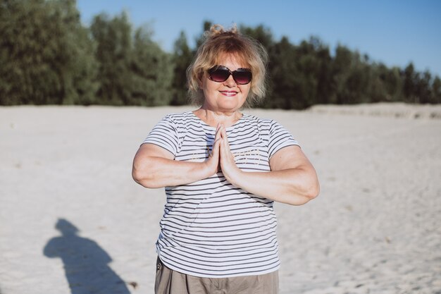 Ältere Frau, die Yogaübungen im Strand im Sand tut