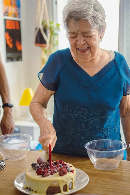 Ältere Frau genießt es, ihren eigenen Geburtstagskuchen zu schneiden, der mit weißer Schokolade und Beeren bedeckt ist