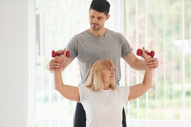 Ältere Frau hat einen Besuch in der Klinik und Rehabilitation Männlicher Ausbilder hilft ihr