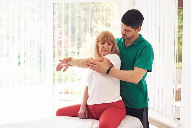 Ältere Frau hat einen Besuch in der Klinik und Rehabilitation Männlicher Ausbilder hilft ihr