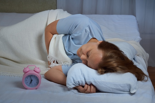 Ältere Frau im blauen Pyjama hat die Zeit durchgeschlafen, sie leidet an Schlaflosigkeit.