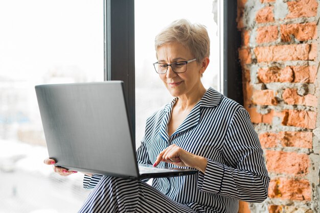 Ältere Frau im Pyjama, die an einem Laptop arbeitet