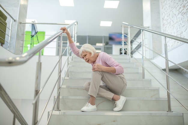 Ältere Frau im rosa Hemd, das auf die Treppe fällt