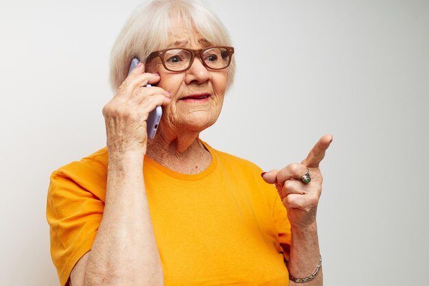 Ältere Frau in einem gelben T-Shirt, das Kommunikation per Telefon vor hellem Hintergrund aufwirft