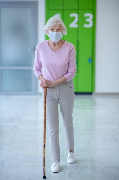 Ältere Frau in einer Gesichtsmaske, die im Korridor geht