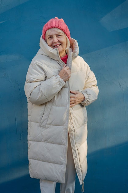 Ältere Frau in trendiger Oberbekleidung. Alte Frau in gestricktem rosa Hut, die lächelt und warmen Mantel anpasst