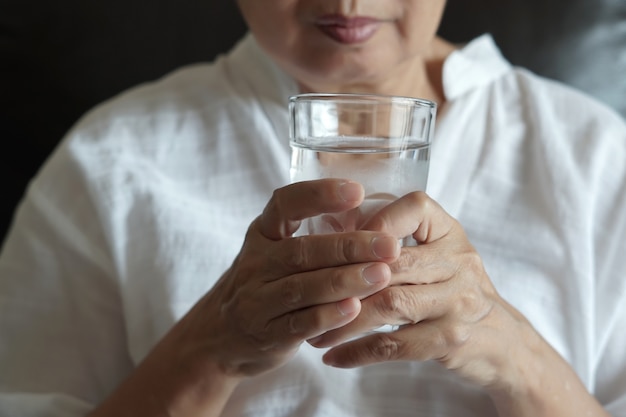 Ältere Frau isst Medizin und mit Pillen und Glas Wasser zu Hause