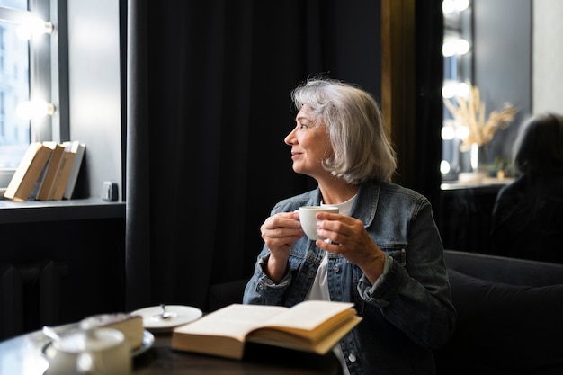 Ältere Frau liest ein Buch und trinkt Kaffee in einem Café