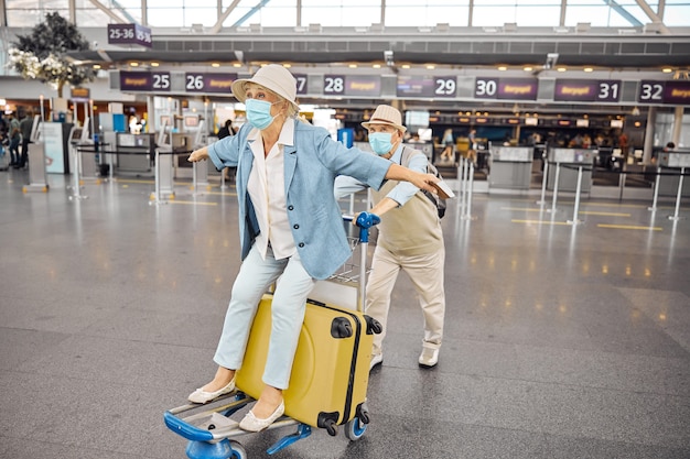 Ältere Frau mit ausgestreckten Armen genießt ihre Fahrt auf einem Gepäckwagen am Flughafenterminal