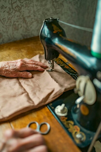 Ältere Frau mit Brille verwendet Nähmaschine faltige Hände der alten Näherinälteren Frau Alte Nähmaschine Klassische manuelle Nähmaschine im Retro-Stil, die für Näharbeiten bereit ist